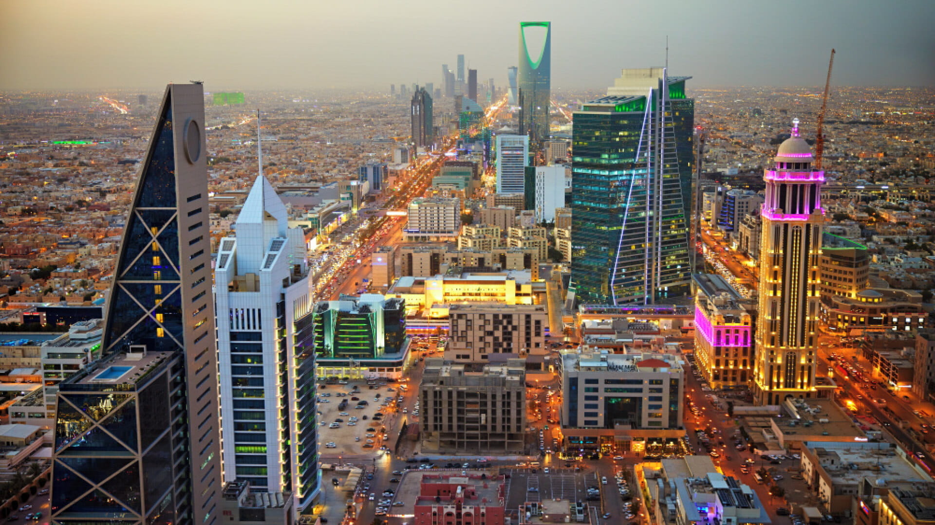 City skyline in the Kingdom of Saudi Arabia featuring modern skyscrapers, illuminated streets, and high-rise buildings at dusk.