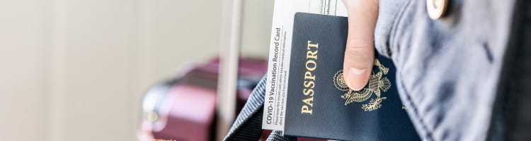 Hand holding passport and approved vaccination card with laptop bag ready for business trip.